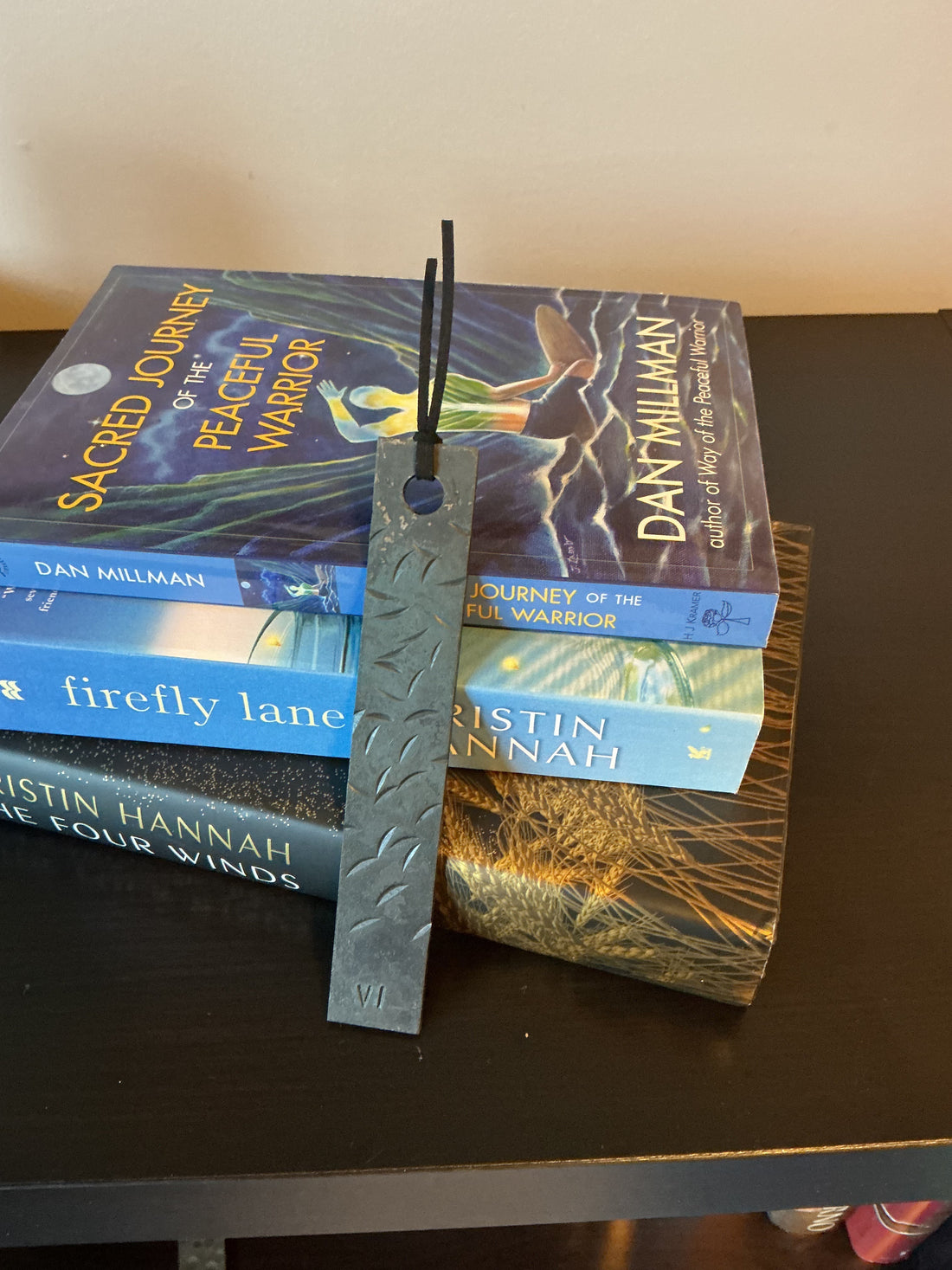 A metal iron anniversary bookmark with distressed pattern, natural finish.Resting against a stack of books,