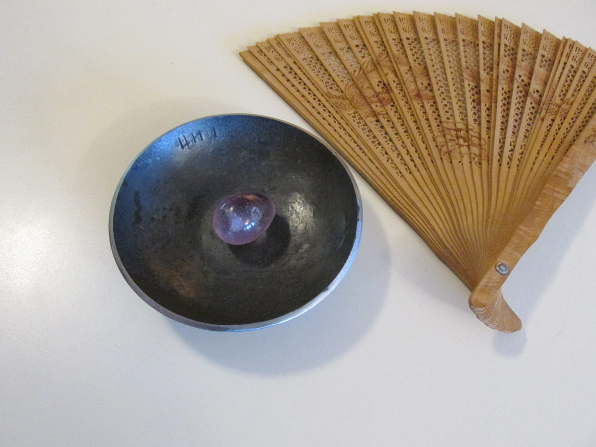 Personalized iron 6th anniversary bowl with tally marks holding purple stone beside carved wood fan