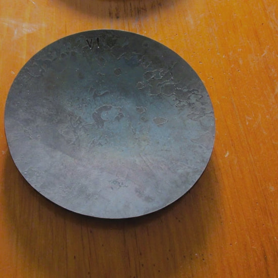 a woman picks up a steel anniversary dish  as she touches and admires the rustic steel finish.